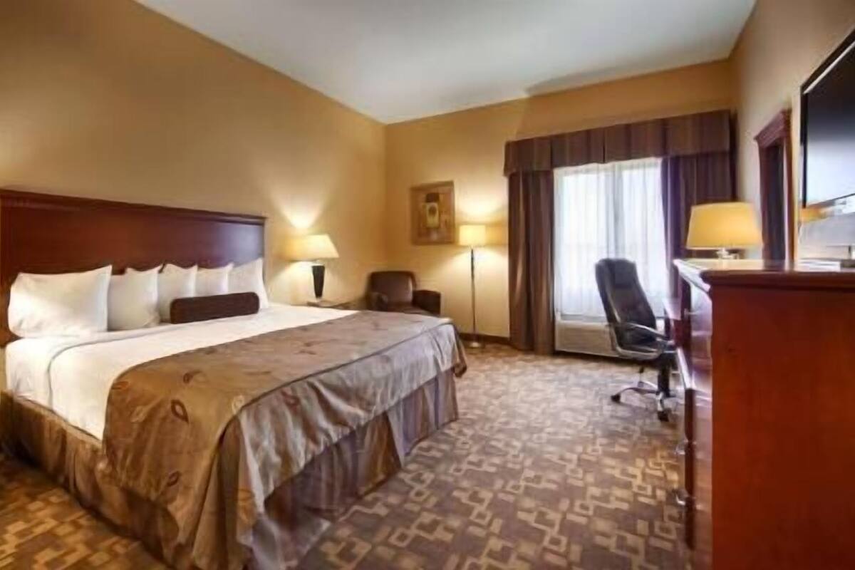 Una habitación de hotel con una cama grande, un escritorio, una silla y una ventana con cortinas.