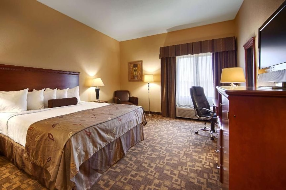 A hotel room with a large bed, two bedside tables, a desk, a chair, and a television.