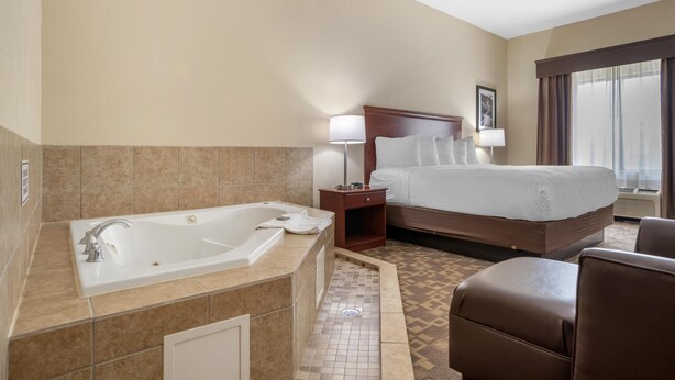 A hotel room with a large bathtub, a bed with a headboard, a nightstand, a lamp, and a window with curtains. - Best Western Opp Inn (Opp)