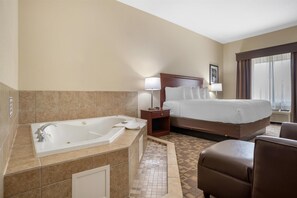A hotel room with a large bathtub, a bed with a headboard, a nightstand, a lamp, and a window with curtains. - Best Western Opp Inn (Opp)