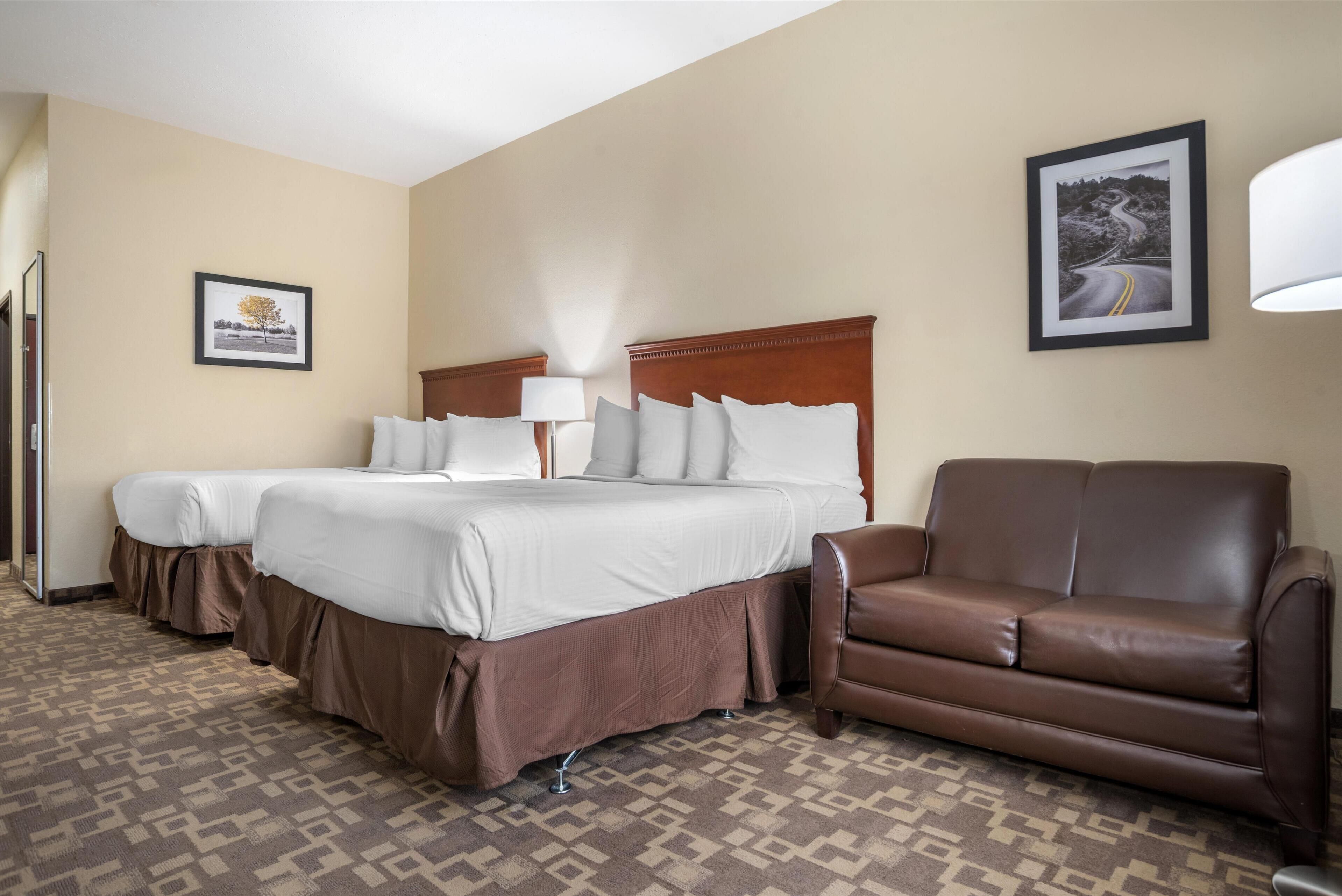 A hotel room with two beds, a brown leather sofa, patterned carpet, and framed pictures on the walls.