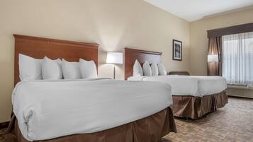 Habitación de hotel con dos camas, cada una con ropa de cama blanca y cabeceros marrones. Hay una mesita de noche con una lámpara entre las camas y un cuadro enmarcado en la pared.
