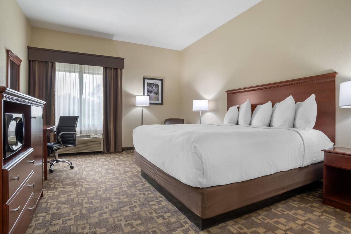Habitación de hotel con una cama grande, un escritorio con silla, cómoda y ventana con cortinas.