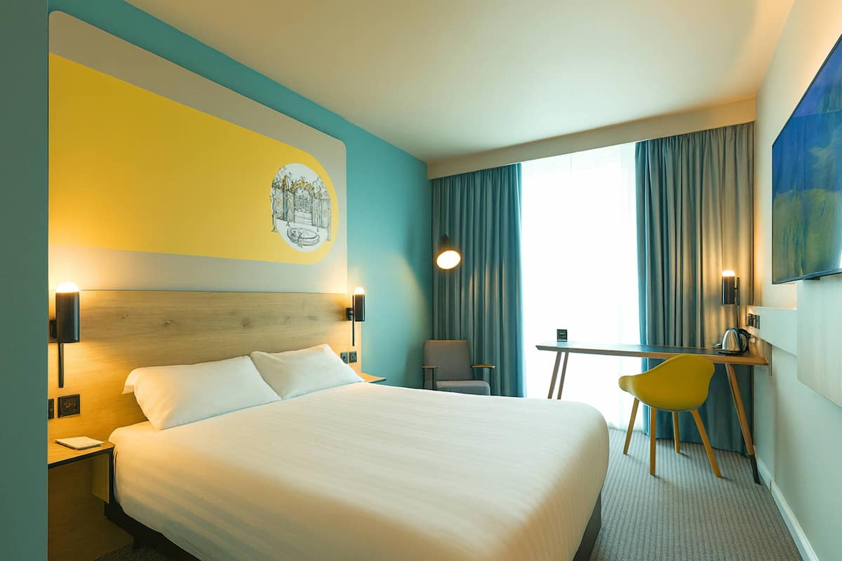 Een hotelkamer met een bed, een bureau, een stoel en een schilderij aan de muur.