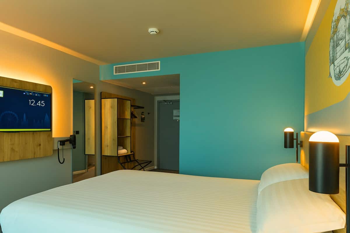 Een moderne hotelkamer met een groot bed, een digitale klok, een telefoon en een zichtbare badkamer door een open deur.
