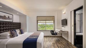 A modern hotel room with a large bed, a desk, a chair, a television, and a window with a view.