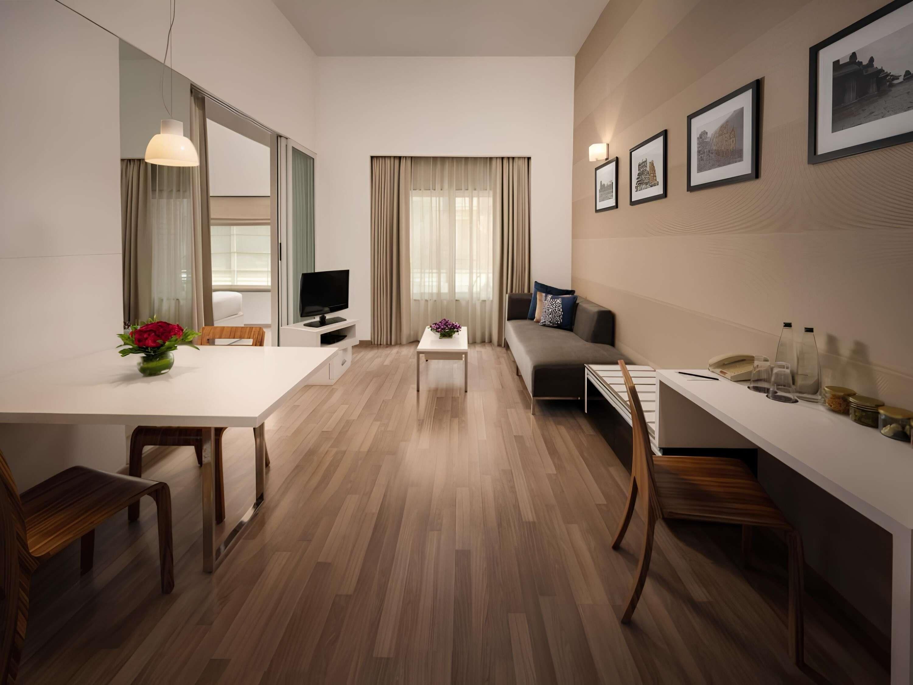 A modern hotel room with a dining area, a sofa, a TV, and framed pictures on the wall.