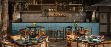 Un restaurante con sillas y mesas de madera, y una zona de bar con estantes llenos de botellas.