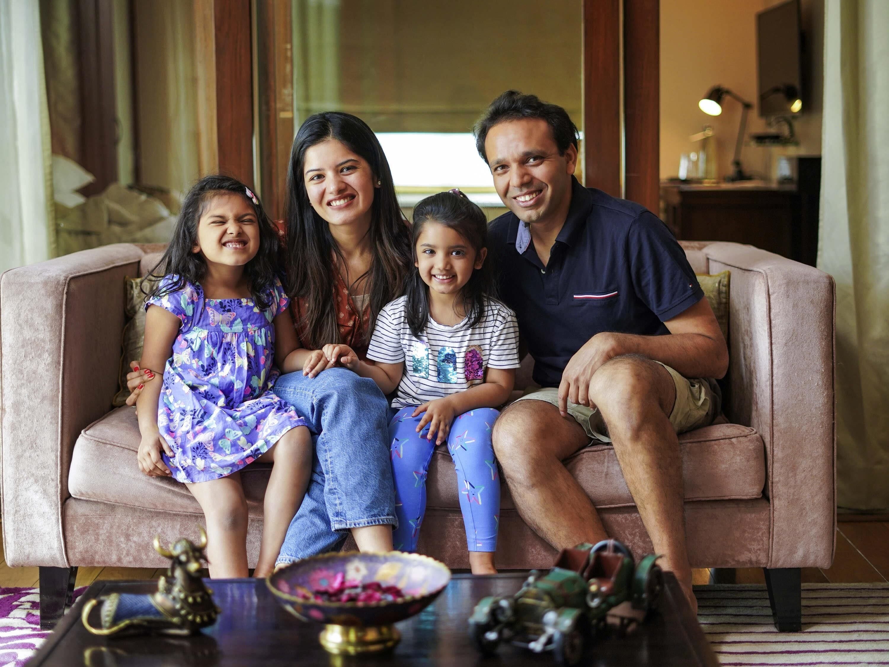 A family of four seated on a sofa in a well-lit room with a coffee table in the foreground.