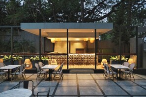 Un área de comedor al aire libre con mesas y sillas, una zona de estar cubierta y vistas a los árboles circundantes.