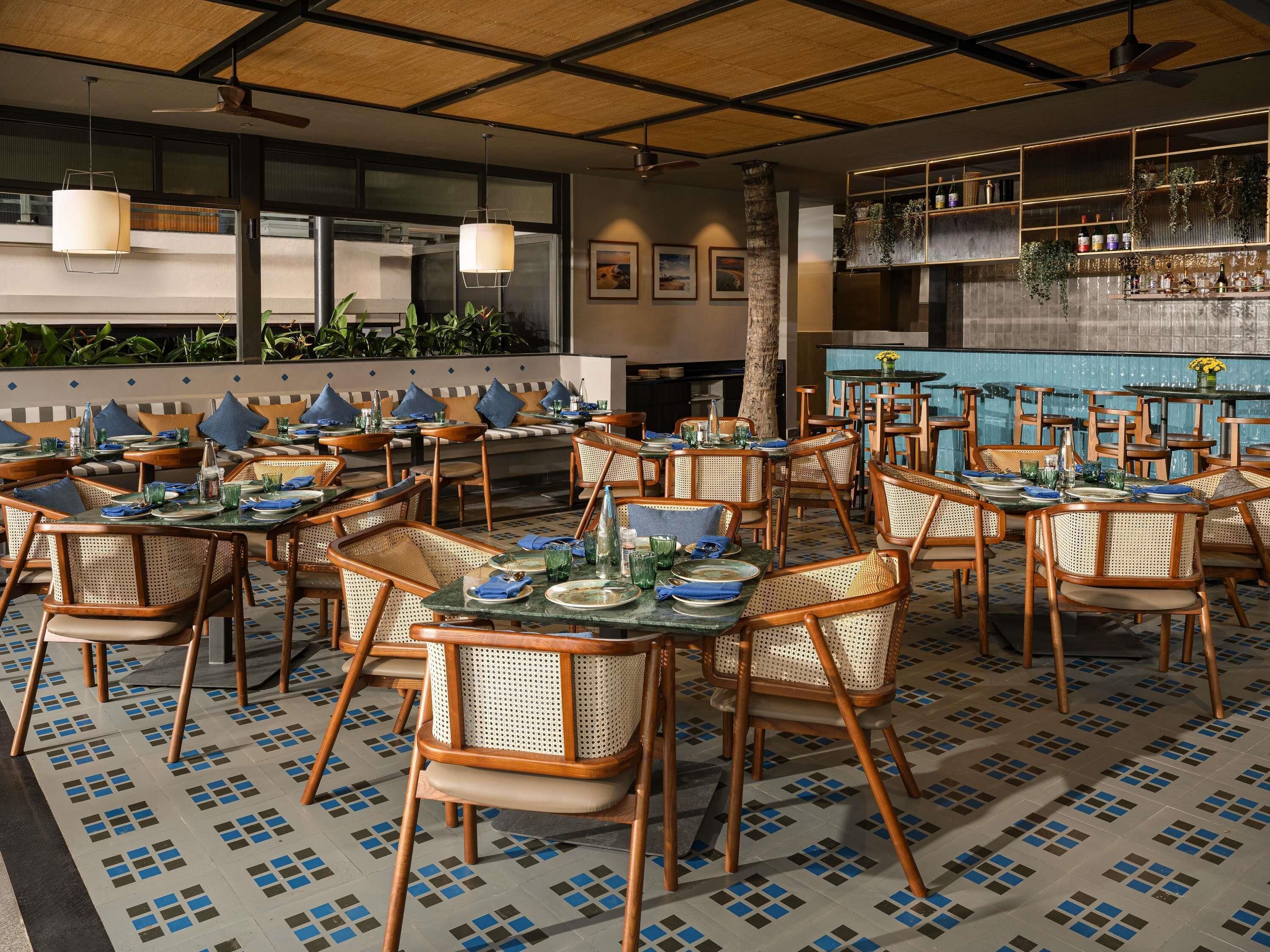 Un restaurant avec des tables rondes, des chaises en osier et un sol carrelé.