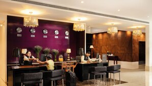 A hotel reception area with a purple wall, multiple clocks, and chandeliers. - Grand Mercure Bangalore (Bengaluru)