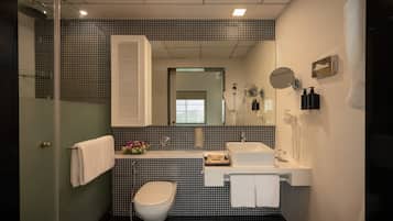 A bathroom with a toilet, sink, mirror, and shower.