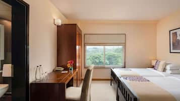 A hotel room with a desk, chair, two beds, a window with a view, and a cabinet.