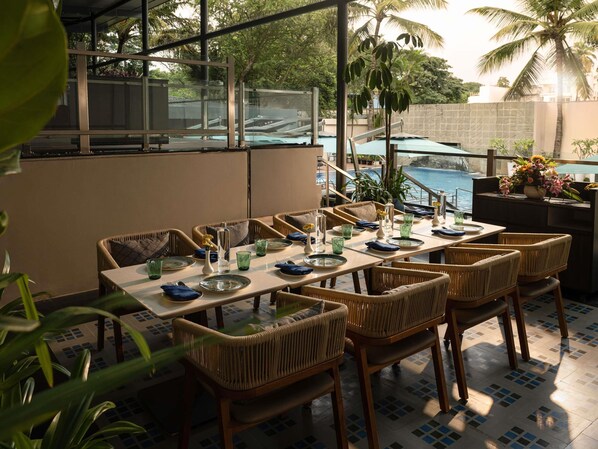 Comedor con sillas de mimbre y una mesa dispuesta para cuatro, con vista a una piscina.
