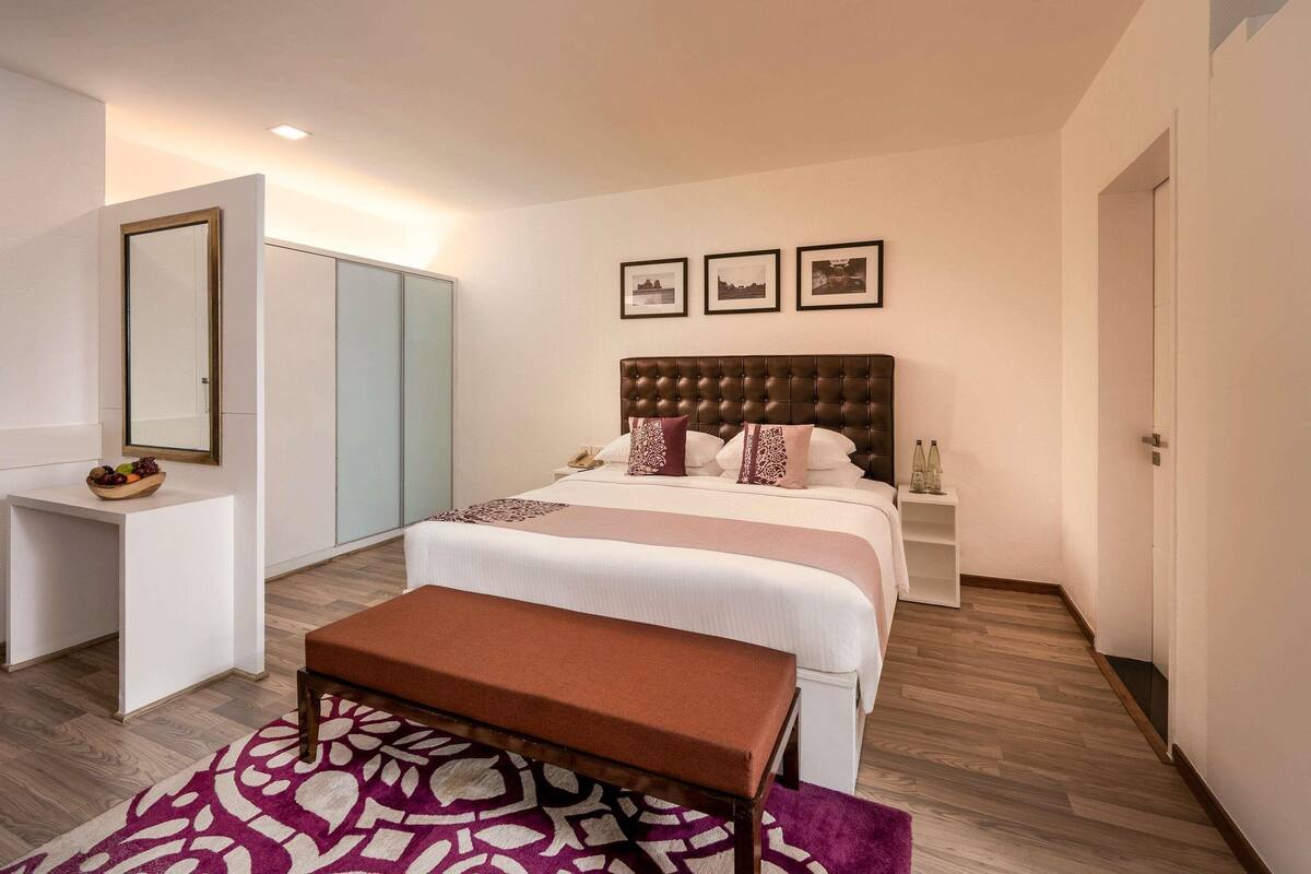A hotel room with a large bed, a bedside table, a wardrobe, and a bench.