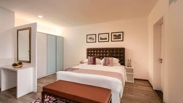 A hotel room with a large bed, a bedside table, a wardrobe, and a bench.