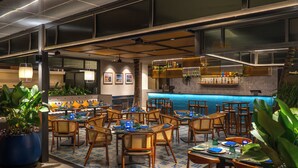 A restaurant with multiple tables and chairs, a bar area, and potted plants. - Grand Mercure Bangalore (Bengaluru)