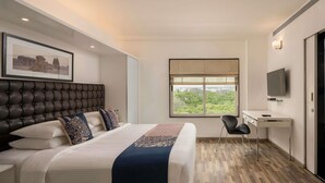 A modern hotel room with a large bed, a desk, a chair, a television, and a window with a view. - Grand Mercure Bangalore (Bengaluru)
