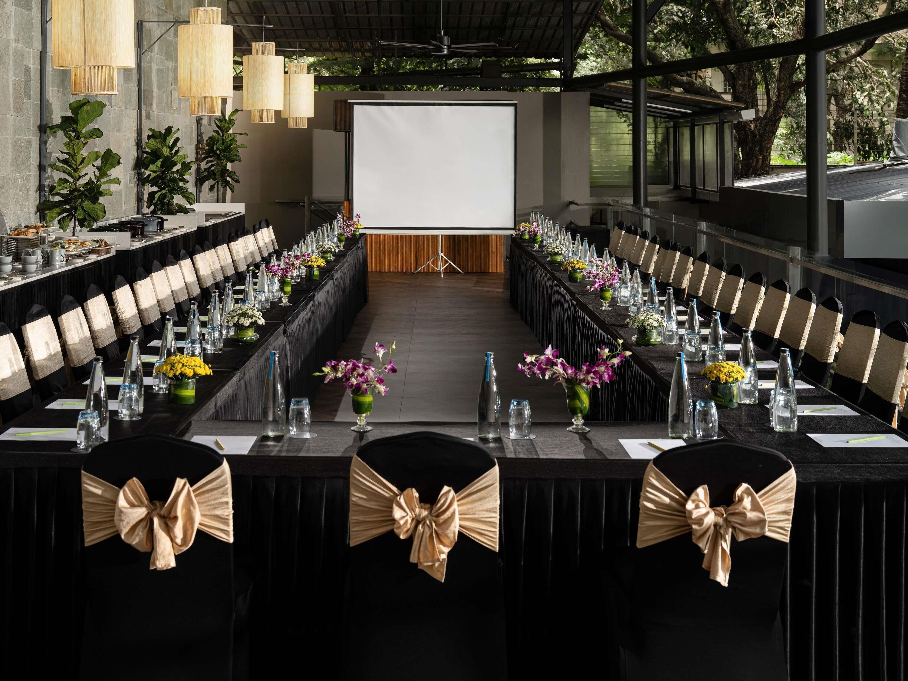 A conference room with a long table, chairs with bow ties, and a projector screen.