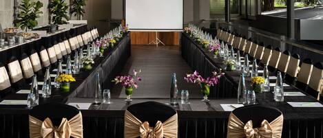 A conference room with a long table, chairs with bow ties, and a projector screen.