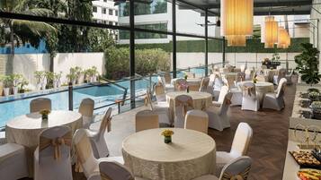 Un espace de restauration aménagé sur le toit, avec des tables rondes, des chaises blanches et une piscine en arrière-plan.