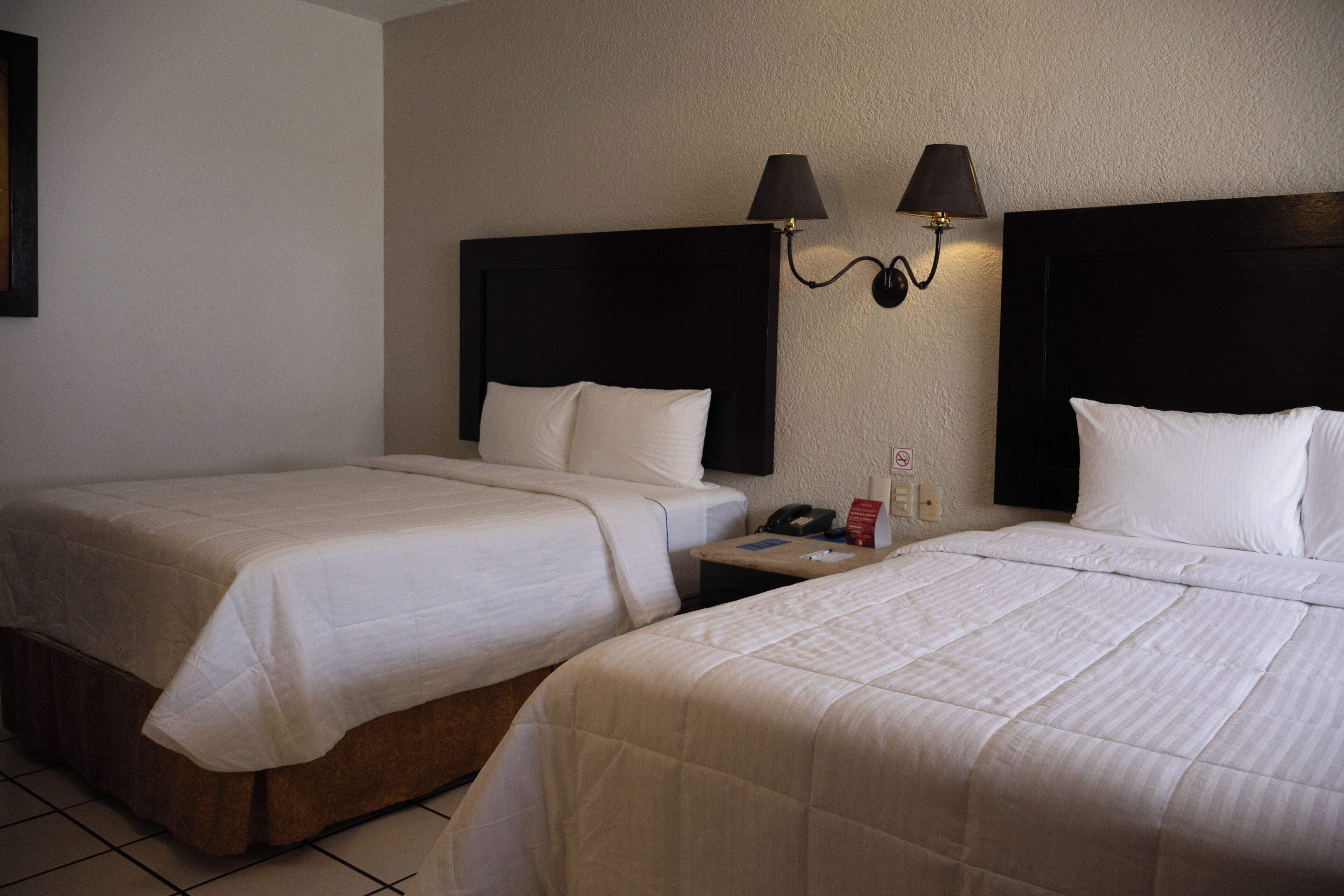 Habitación de hotel con dos camas, una mesita de noche y dos lámparas fijadas a la pared.