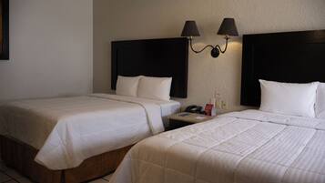 Habitación de hotel con dos camas, una mesita de noche y dos lámparas fijadas a la pared.