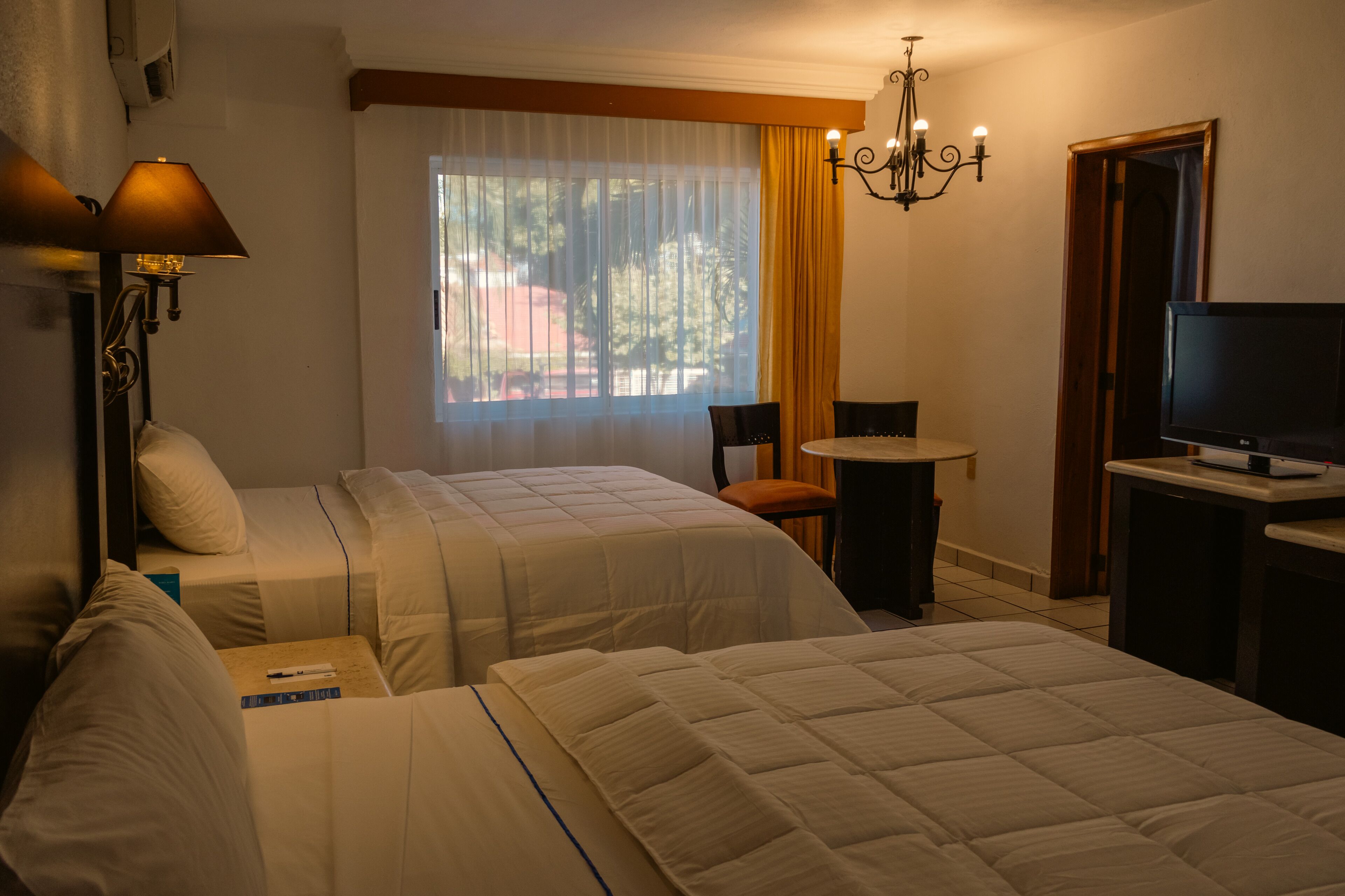 A hotel room with two beds, a desk, a chair, a television, and a window with curtains.