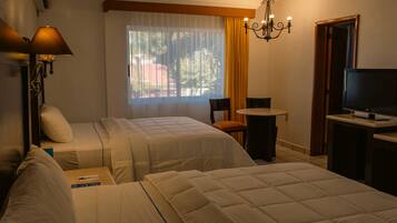 A hotel room with two beds, a desk, a chair, a television, and a window with curtains.