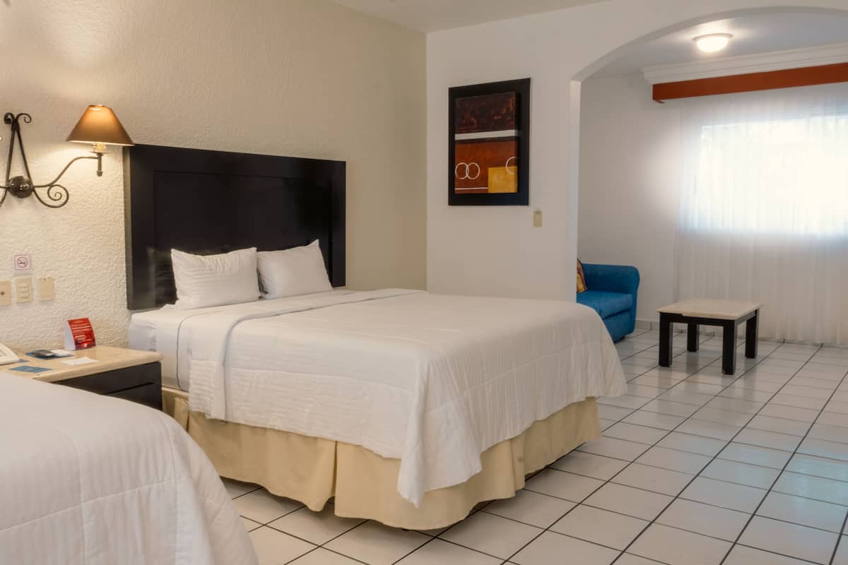 A hotel room with a large bed, a bedside table, a lamp, a chair, and a small table.