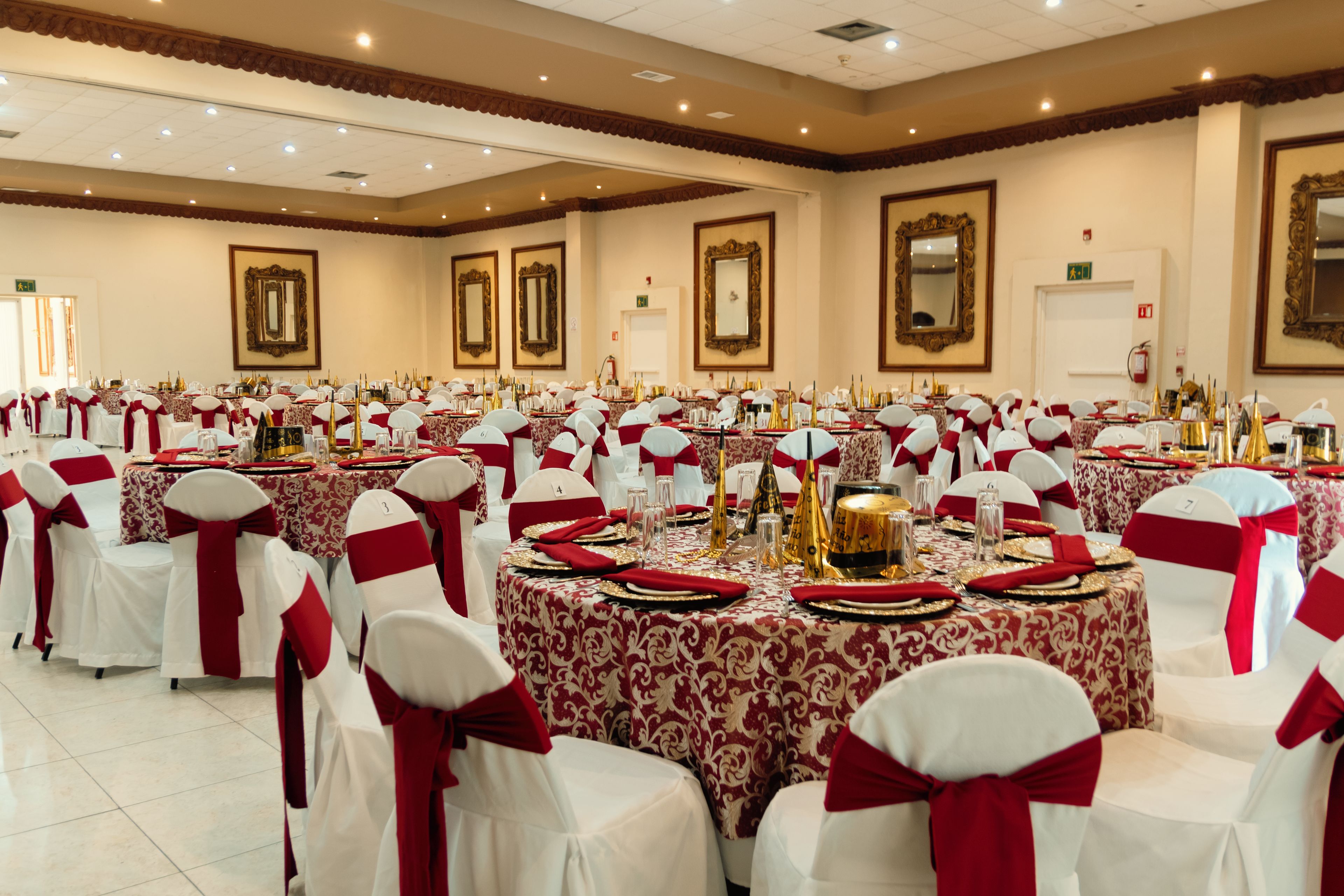 A banquet hall with round tables, white chairs with red sashes, and gold accents.