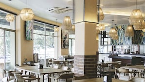 A spacious restaurant with high ceilings, modern pendant lighting, and large windows allowing natural light. Tables and chairs are arranged for dining. - Hotel Maria Isabel (Colima)