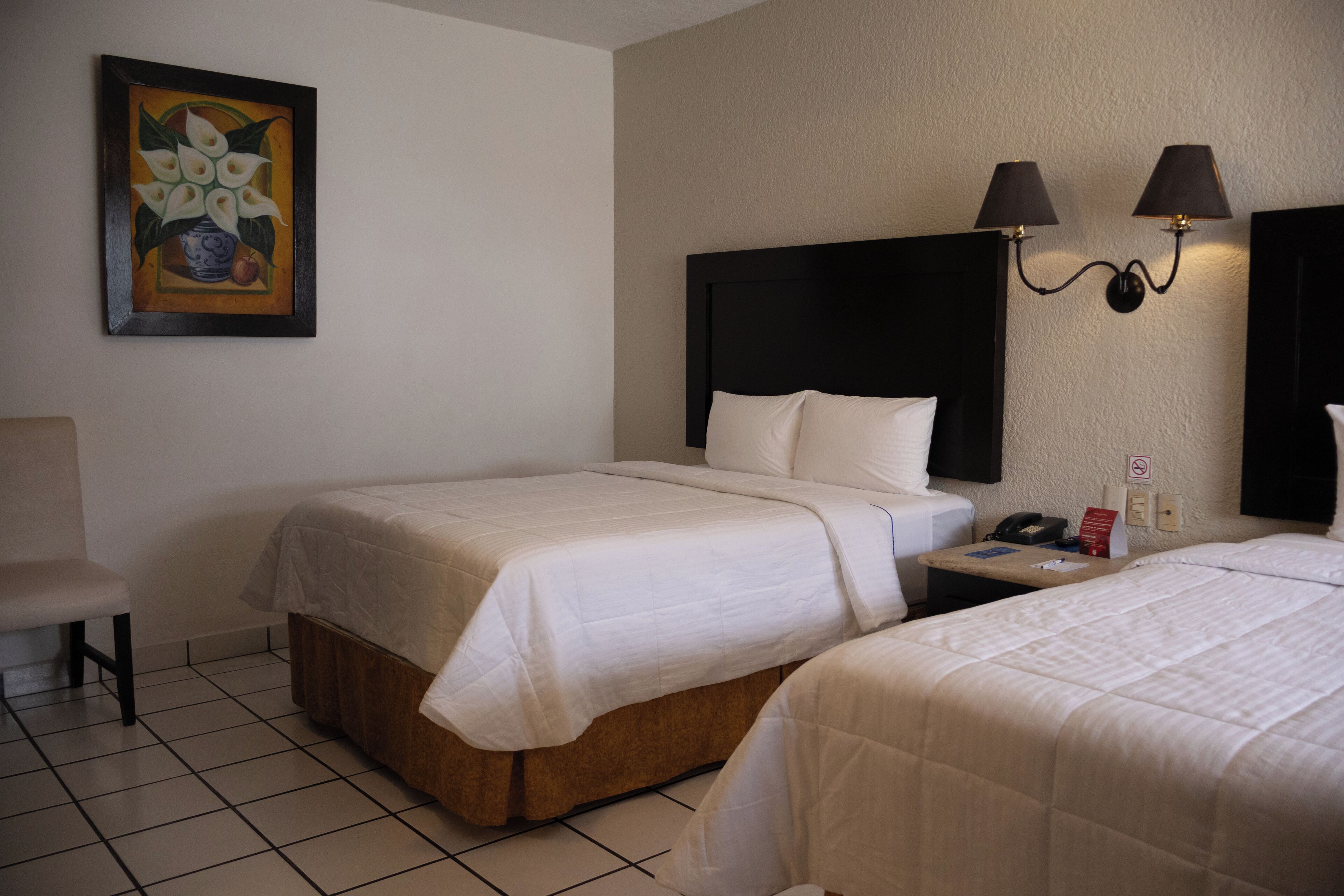 A hotel room with two beds, a nightstand, a chair, and a painting on the wall.