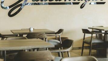 A restaurant interior with tables and chairs, a wall with the name 'Guacamex' in a stylized font, and a small white object on one table.
