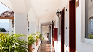 A corridor with potted plants, tiled flooring, and wall-mounted lights. - Hotel Maria Isabel (Colima)