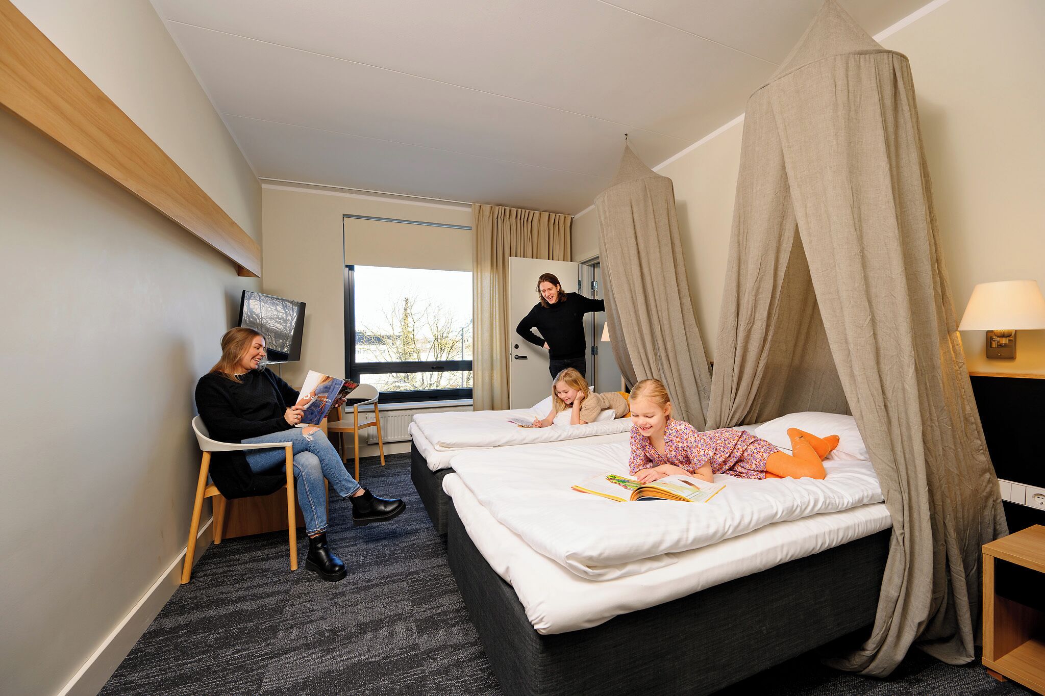 A hotel room with two beds, a TV, a lamp, and a window with curtains.