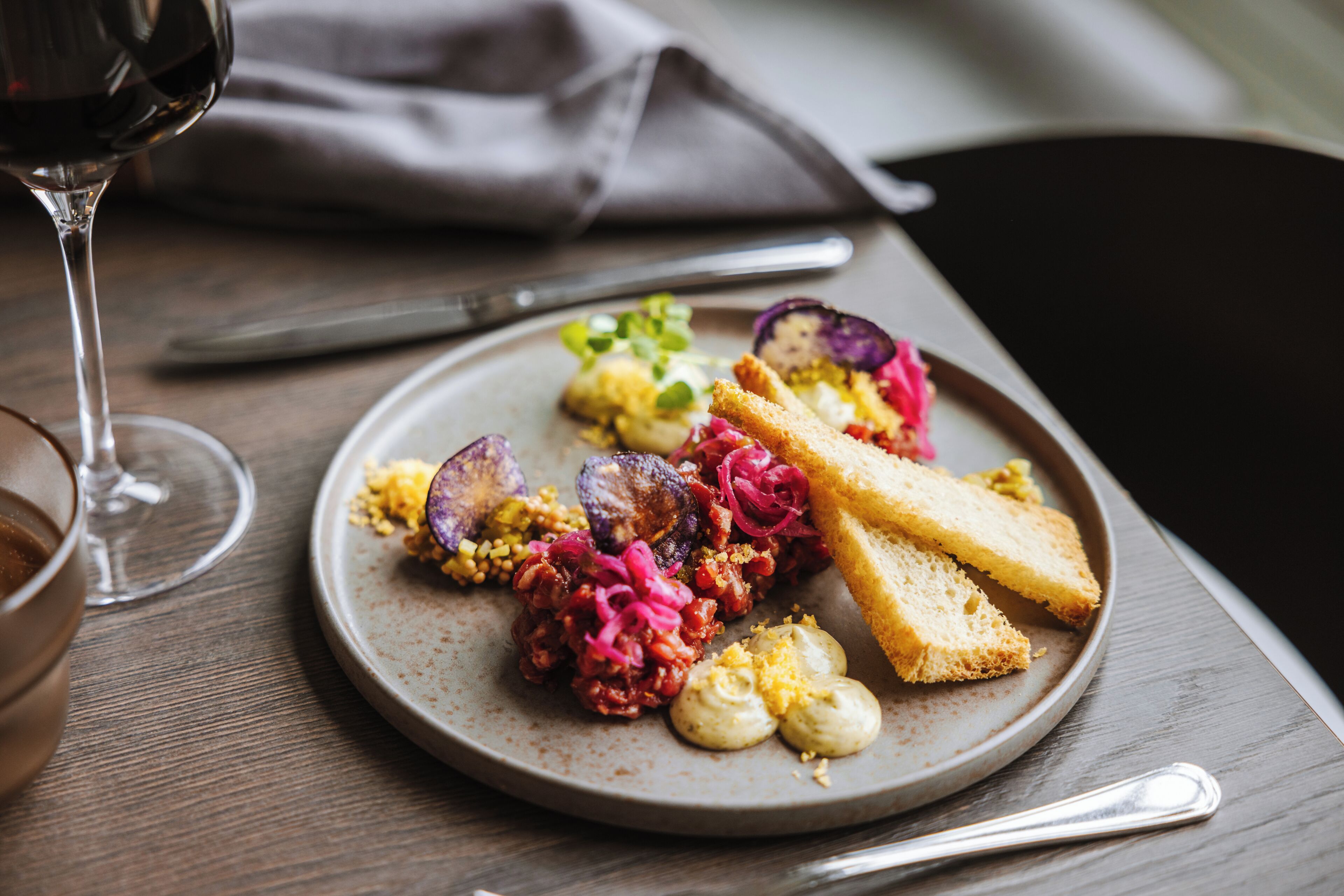 Ein Teller Essen mit Brot, Gemüse und einem Glas Wein auf einem Tisch.