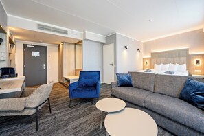 A hotel room with a sofa, armchairs, a small round table, a bed with pillows, a desk with a computer, and a mirror. - Dorpat Hotel (Tartu)
