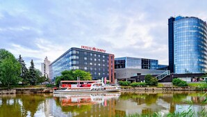 Un hotel moderno con fachada de vidrio, un río al frente y un barco fondeado cerca.