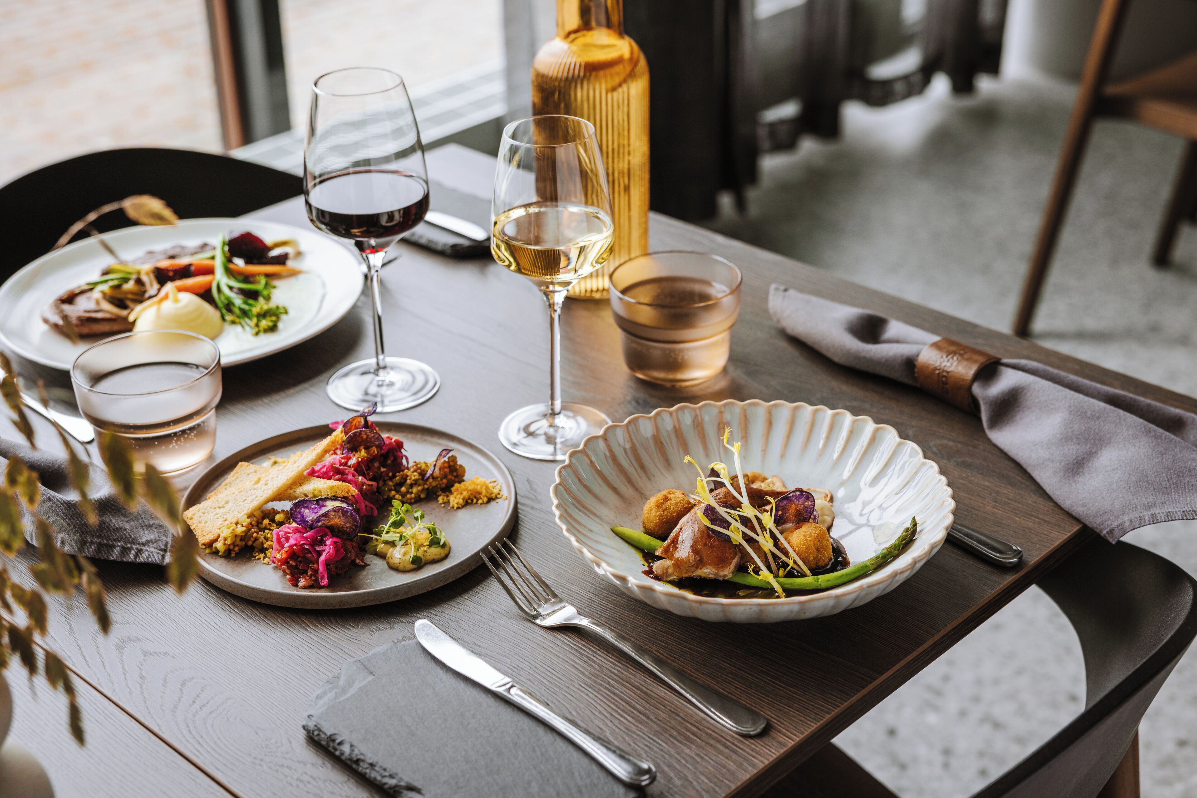 Una mesa de comedor con platos de comida, copas de vino y cubiertos.