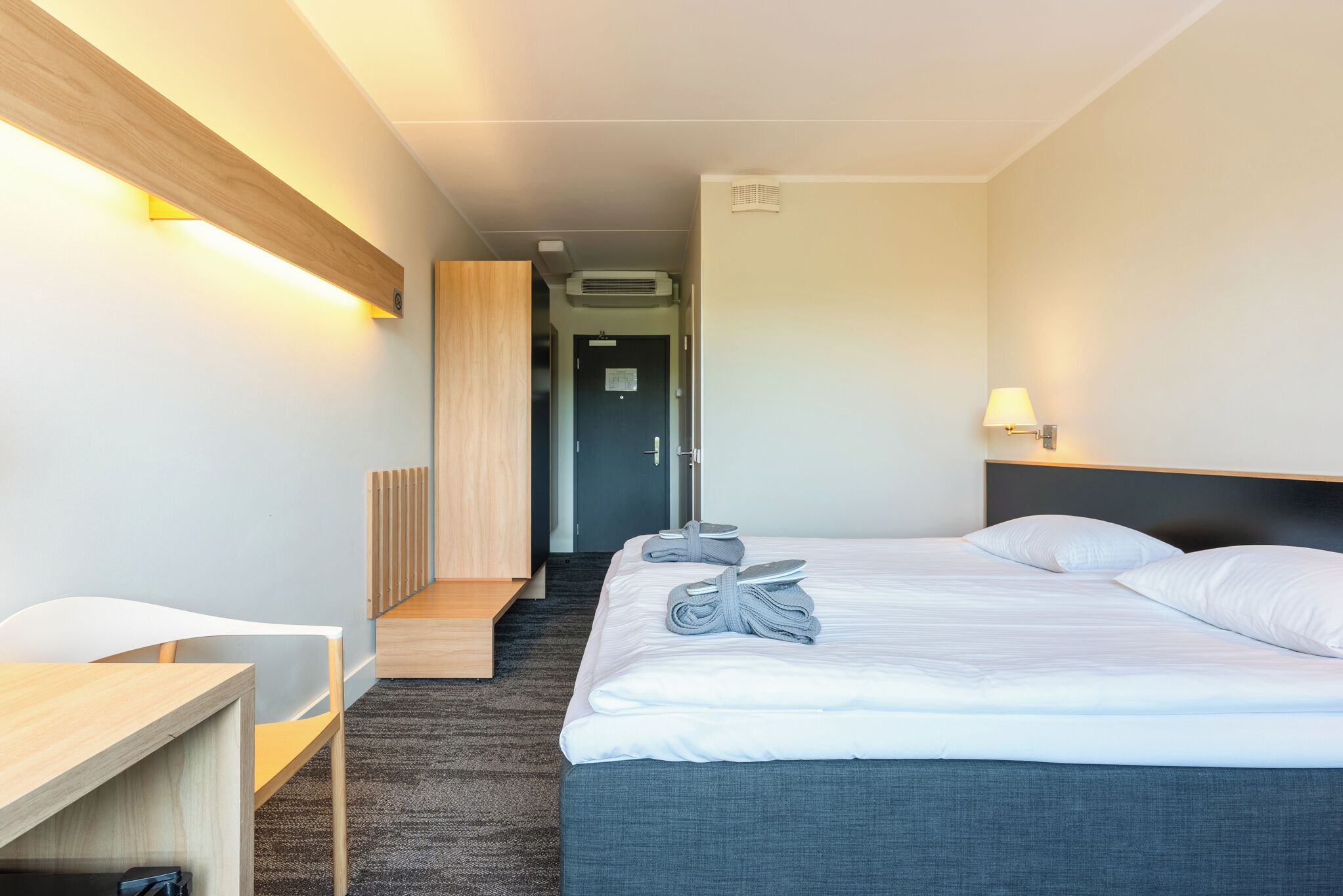 Una habitación de hotel con una cama, un escritorio, una silla, una lámpara y una puerta.