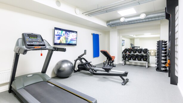 A gym with treadmills, a stationary bike, a rowing machine, and a rack of dumbbells. - Dorpat Hotel (Tartu)