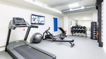 Un gimnasio con cintas de correr, una bicicleta estática, una máquina de remo y un soporte con mancuernas.