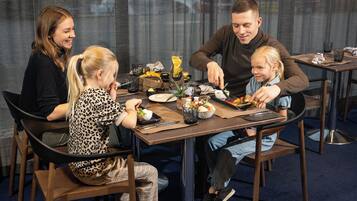 Una familia cenando en un restaurante con una decoración moderna, que incluye un separador de vidrio y una mesa servida con diversos platos y bebidas.