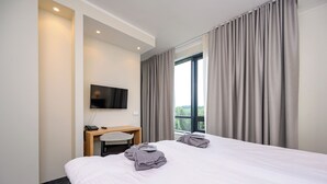 Habitación de hotel con cama, escritorio, silla, televisor y ventana con cortinas.