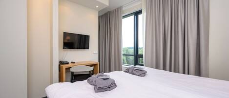 A hotel room with a bed, a desk, a chair, a TV, and a window with curtains.