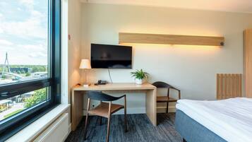 A hotel room with a desk, chair, bed, TV, and a window with a view of a bridge.