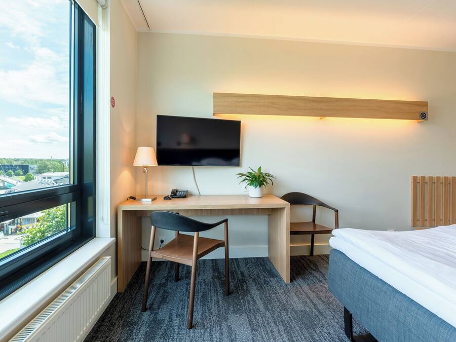 A hotel room with a desk, chair, bed, TV, and a window with a view of a bridge.