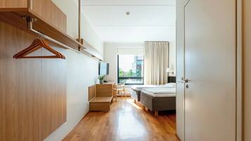 Habitación de hotel moderna con suelo de madera, cama, escritorio con silla, televisor y ventana con cortinas.